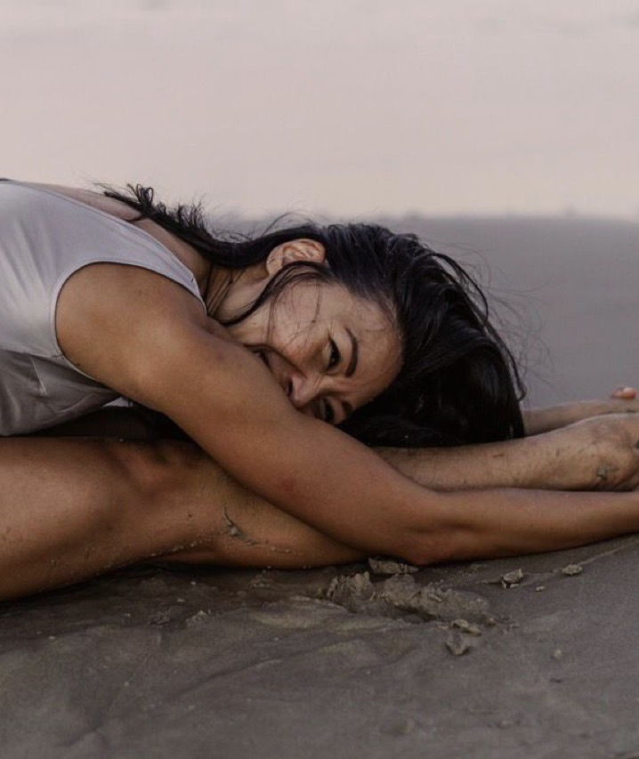 Rebecca Penrose resting in a forward fold on dark volcanic sand