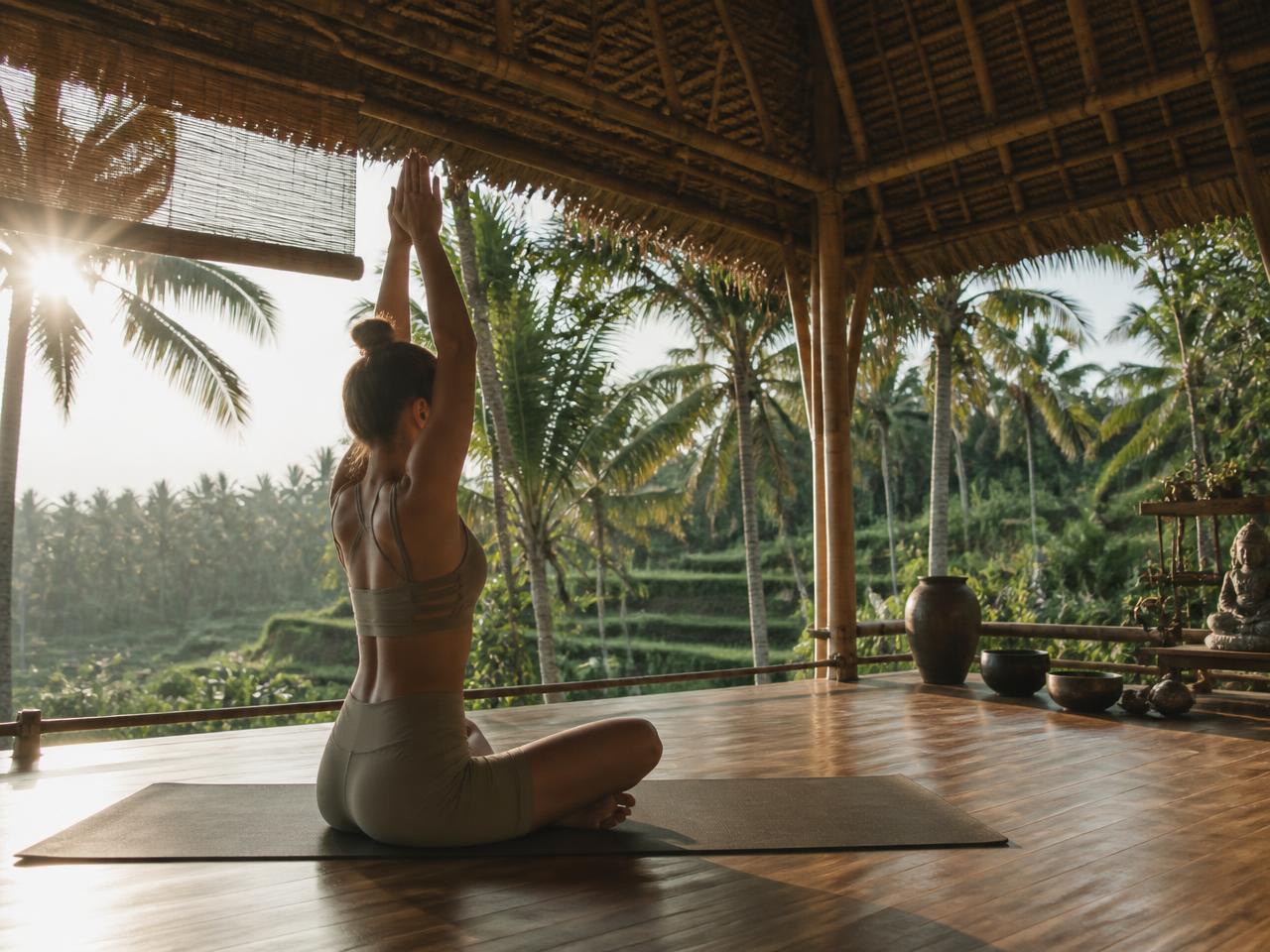 Open bamboo yoga shala surrounded by palms and rice terraces at sunrise
